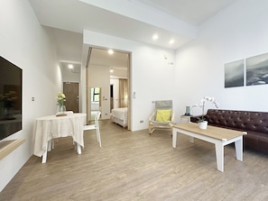 A modern living room with a wooden floor, a sofa, a coffee table, a TV, and a dining area with a table and chairs. - OX Suites (Kaohsiung)