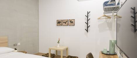A hotel room with a bed, bedside table with a vase of flowers, a desk with a coffee maker, a chair, and wall decorations including animal silhouettes and a leaf pattern.