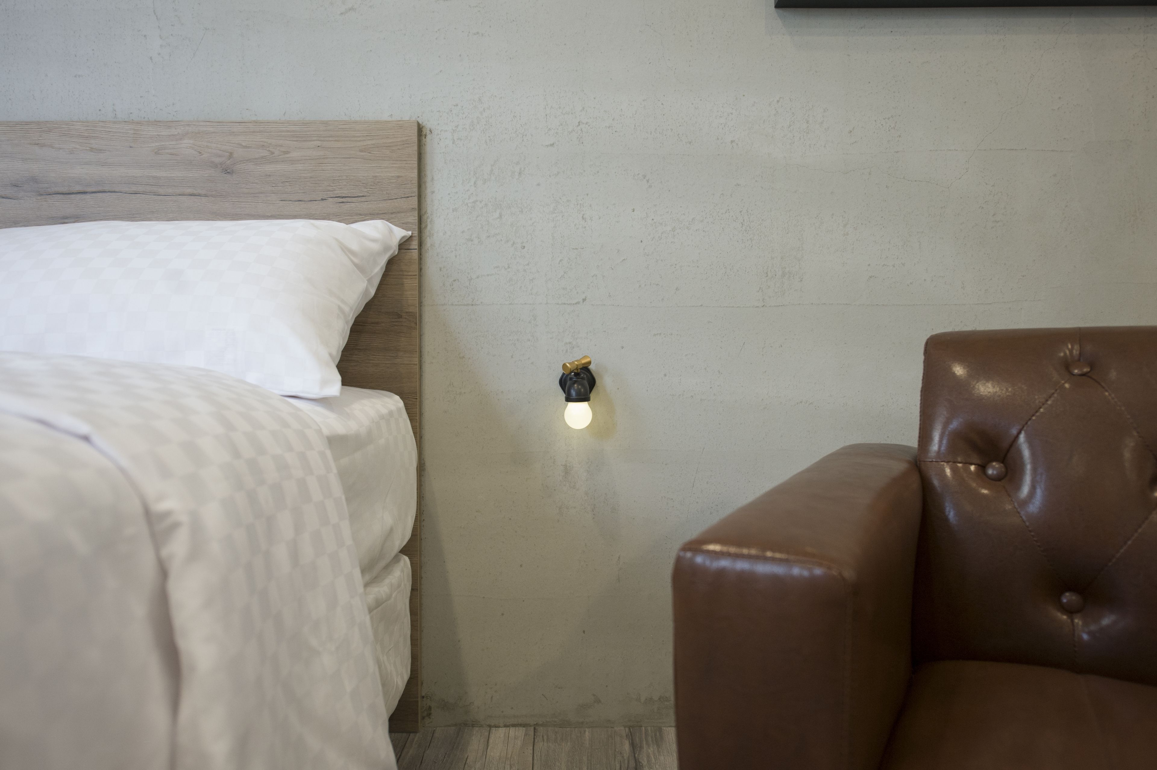 Un dormitorio con cabecera de madera, un sillón de cuero marrón y una lámpara de pared.