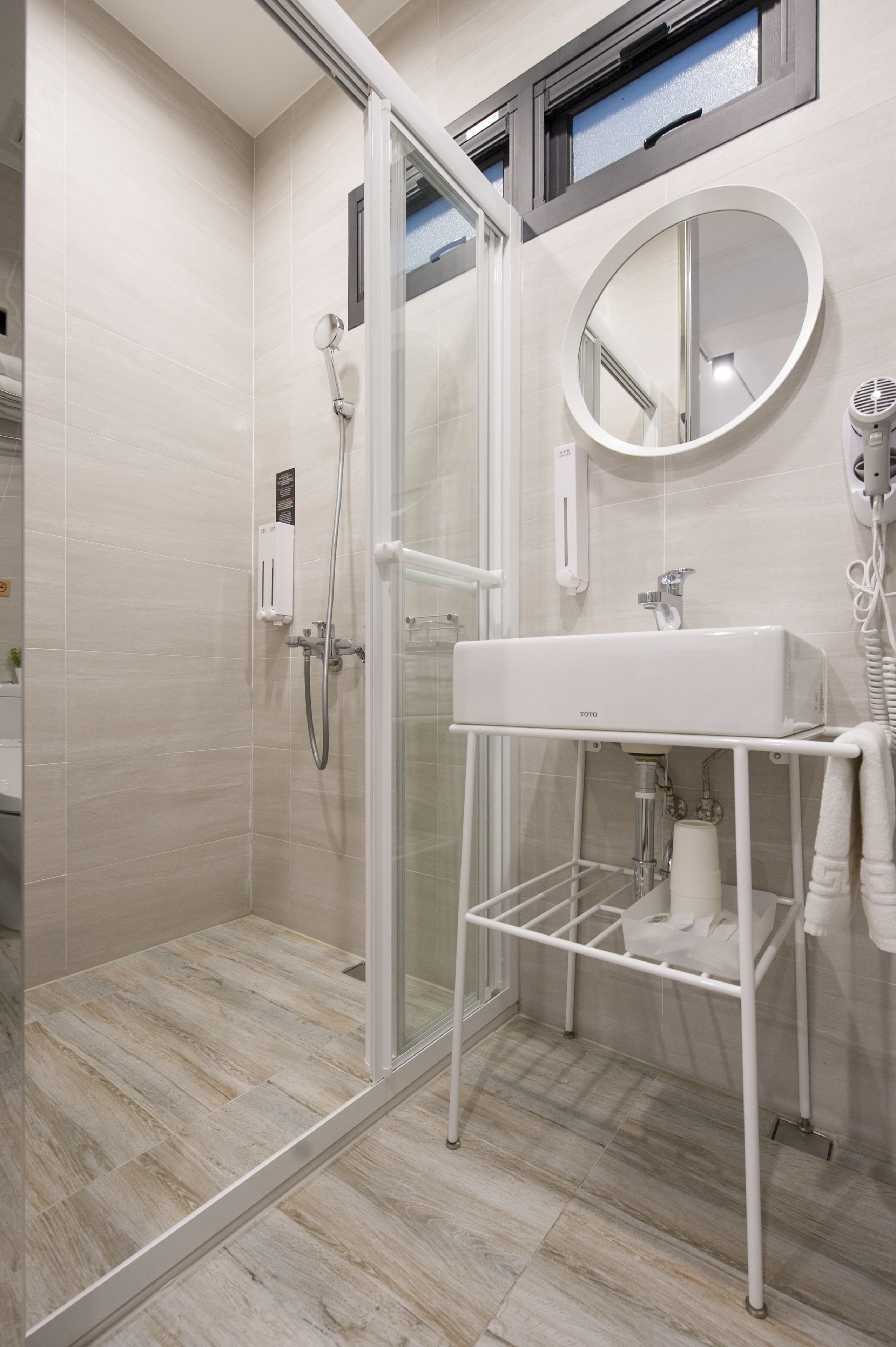 A modern bathroom with a glass shower enclosure, a white sink, and a round mirror.