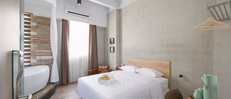Una habitación de hotel moderna con una cama grande, cabecera de madera, un escritorio con silla, una mesita con una planta y aire acondicionado de pared.