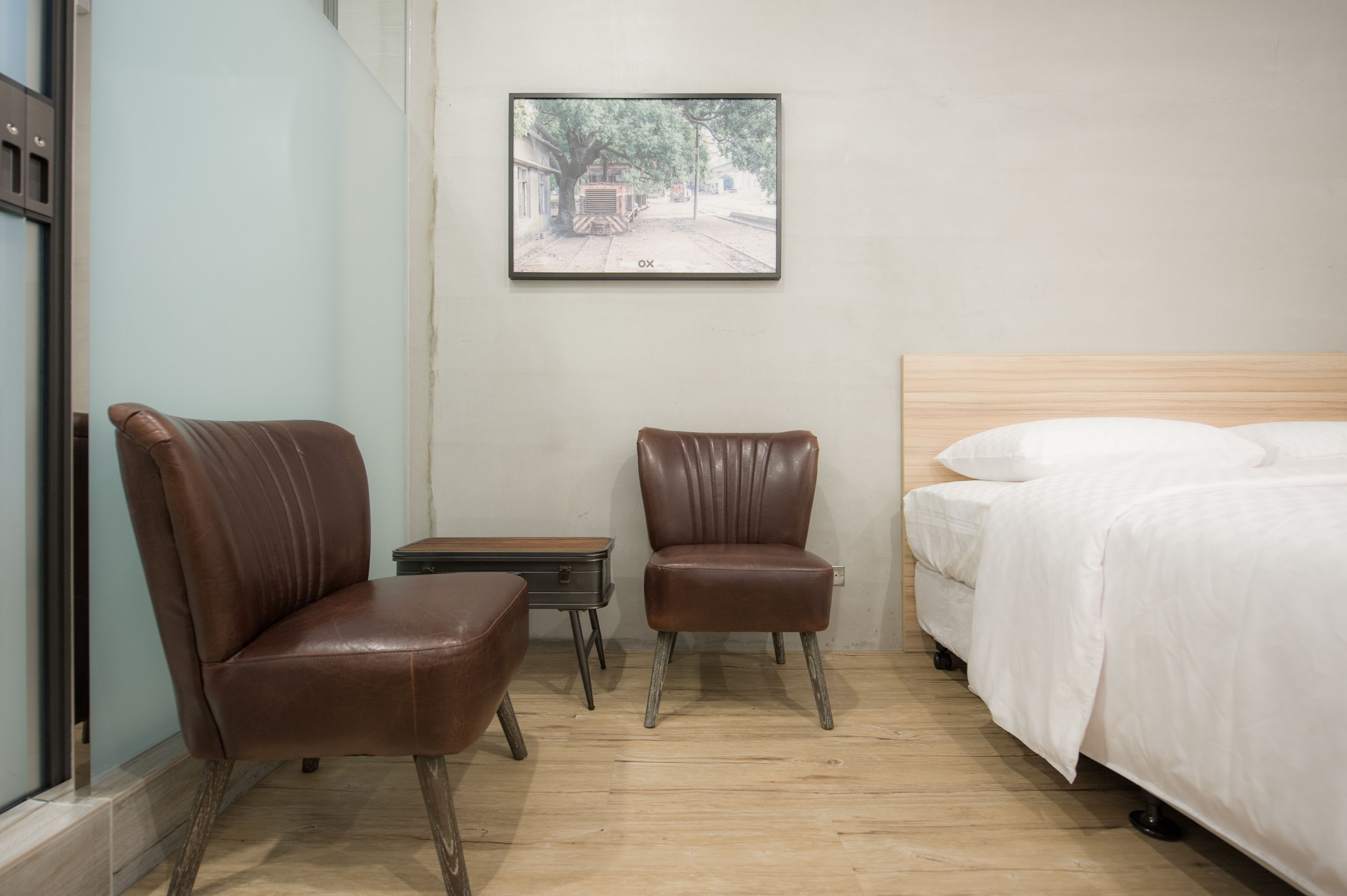Une chambre d’hôtel avec un lit, deux fauteuils en cuir, une petite table et un tableau encadré au mur.
