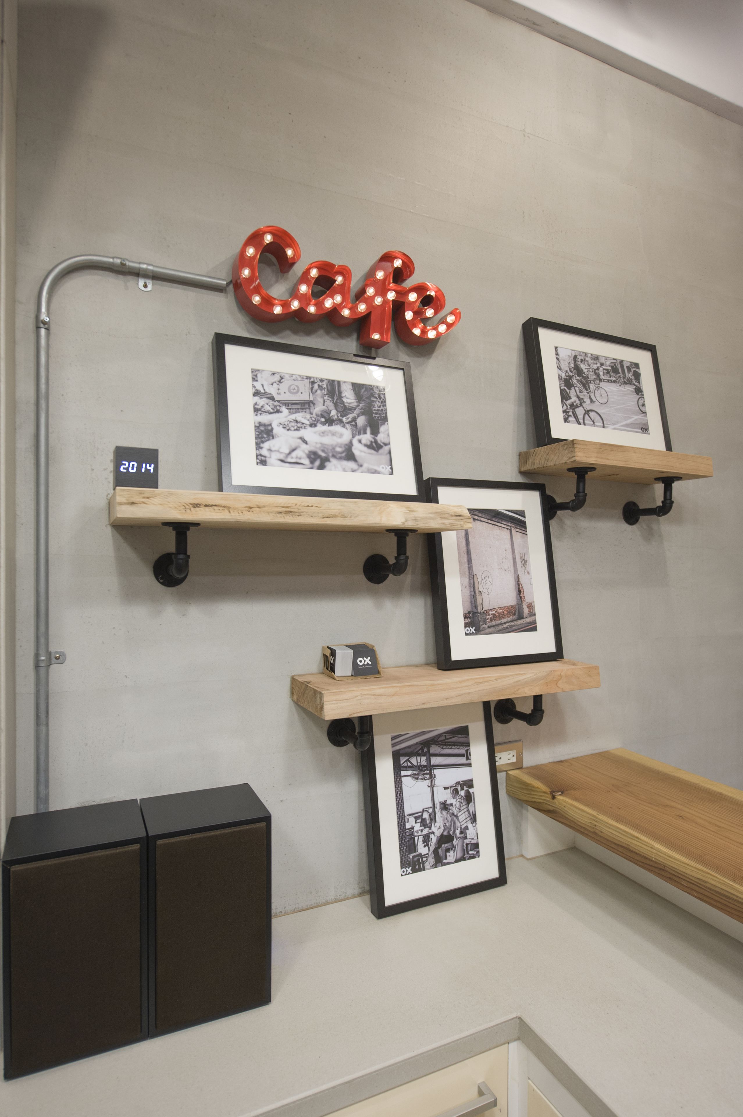 Een muur met een 'Cafe'-bord, ingekaderde foto's en houten planken.