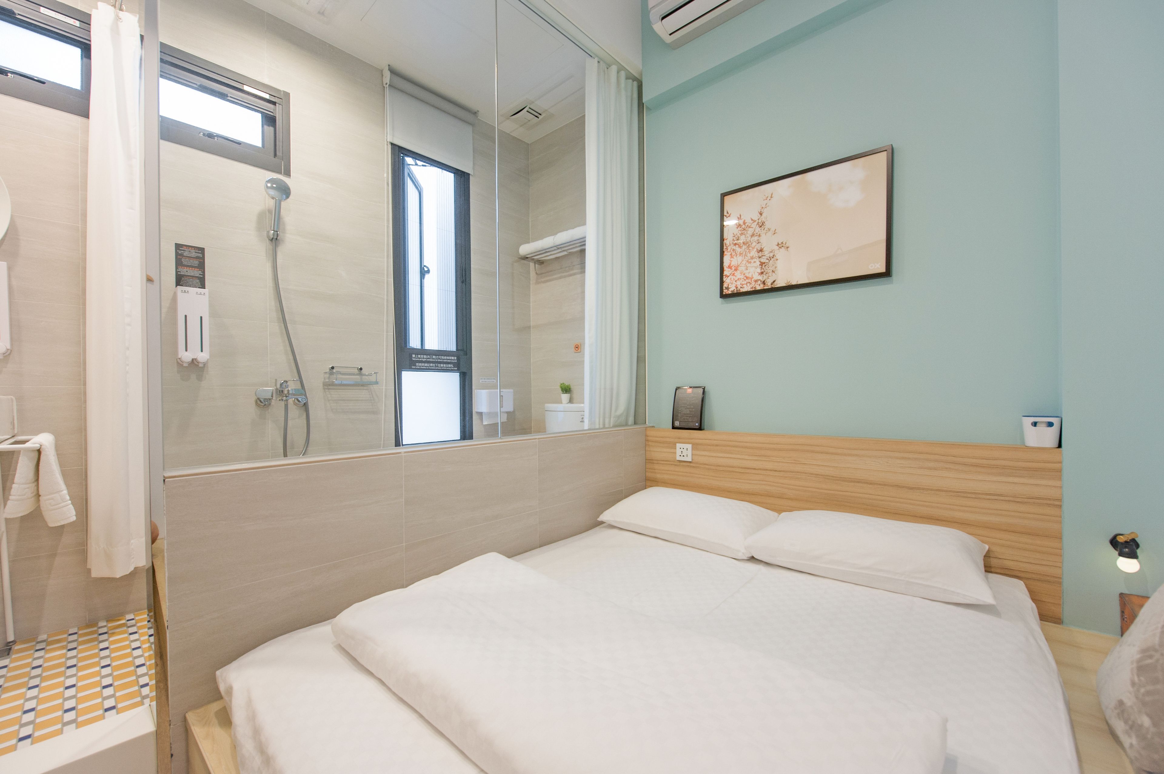 A modern hotel room with a large bed, a shower area, and a wall-mounted artwork.