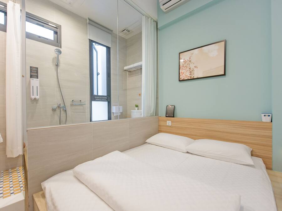 A modern hotel room with a large bed, a shower area, and a wall-mounted artwork.