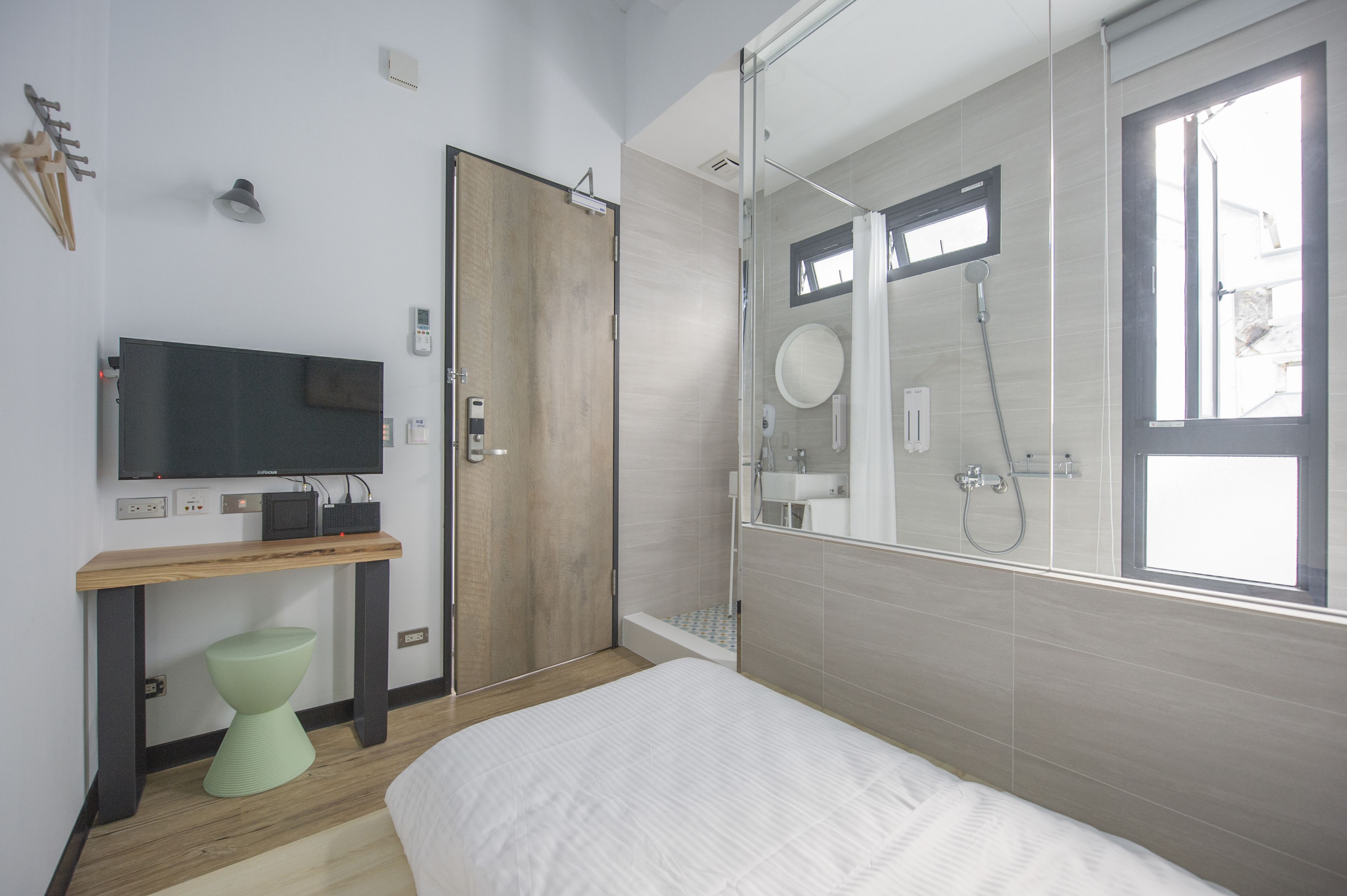 Et moderne hotelværelse med seng, skrivebord med fladskærms-tv, bruseområde med glasdør og et vindue, der giver naturligt lys.
