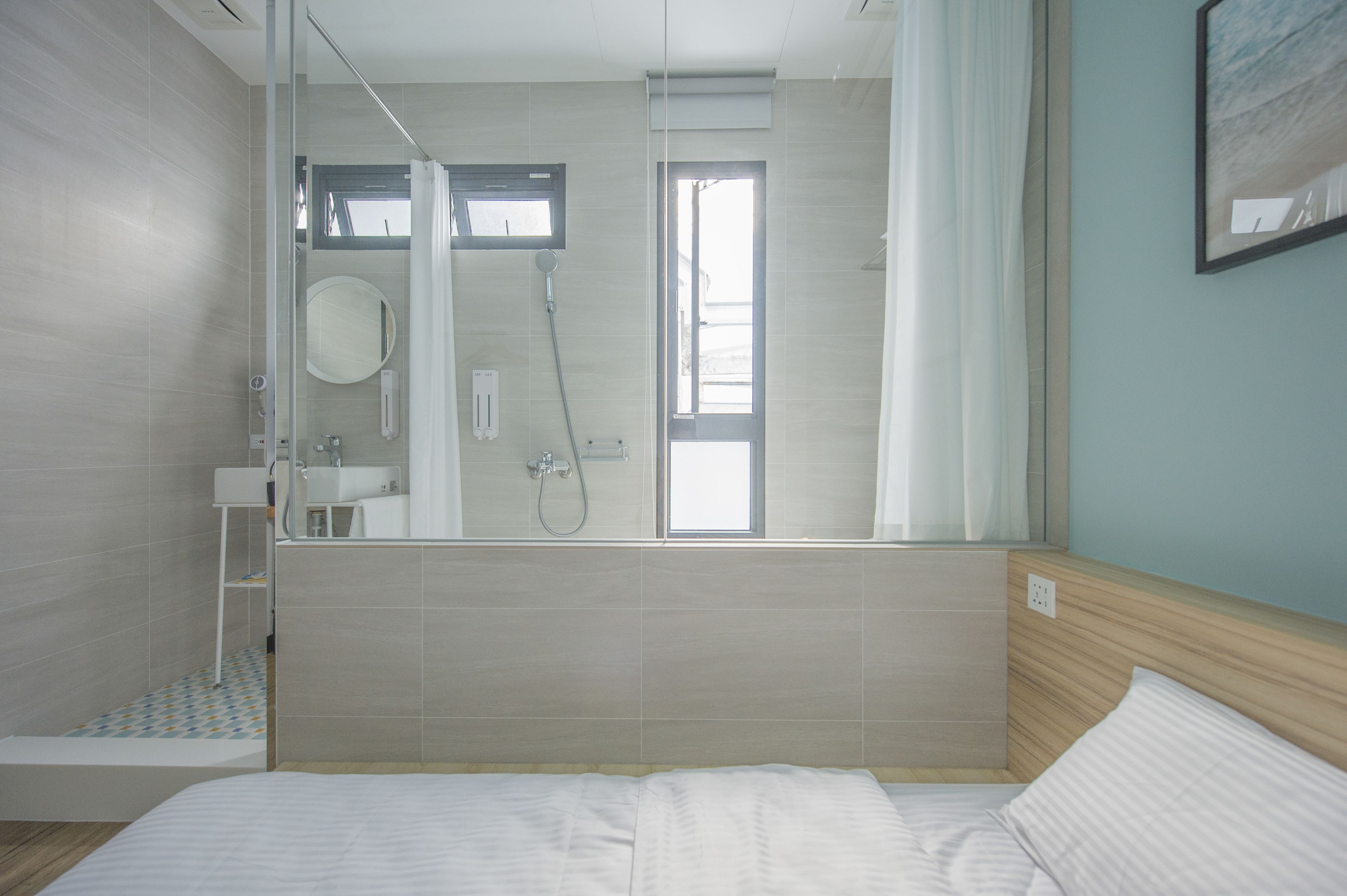 Una habitación de hotel moderna con una cama grande, zona de ducha y baño con espejo y lavamanos.