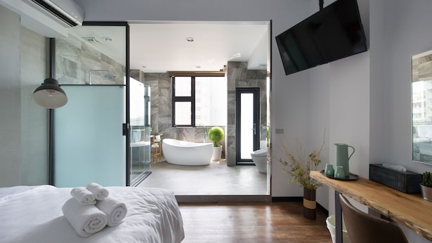 Una habitación de hotel moderna con una cama grande, un escritorio de madera, un televisor de pantalla plana y vistas al baño.