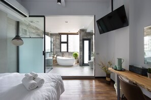 A modern hotel room with a large bed, a wooden desk, a flat-screen TV, and a view into the bathroom. - OX Suites (Kaohsiung)