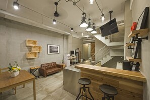 A modern kitchen with a wooden countertop, bar stools, a sofa, and a television mounted on the wall.