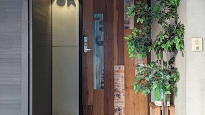 Una entrada moderna con puerta de madera, una lámpara de pared y una planta en maceta.