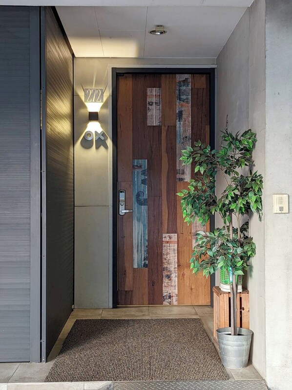 A modern entrance with a wooden door, a wall-mounted light fixture, and a potted plant.