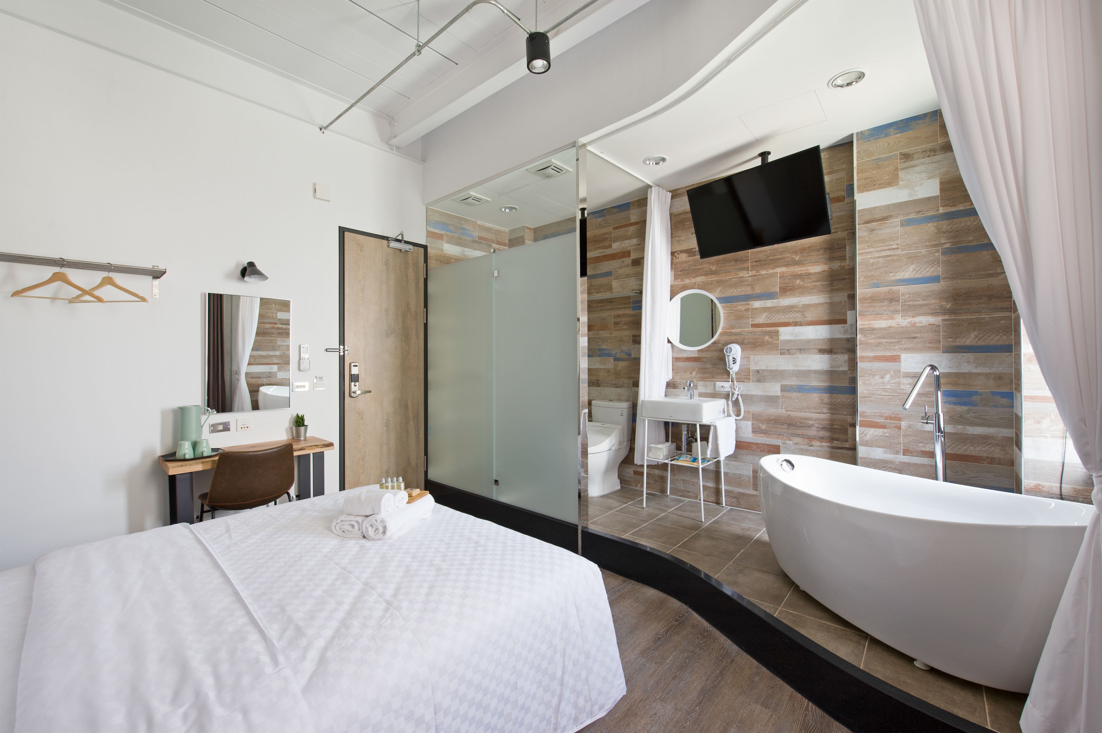 Quarto de hotel moderno com uma cama grande, uma mesa com cadeira, toucador com espelho, banheira e área de chuveiro.