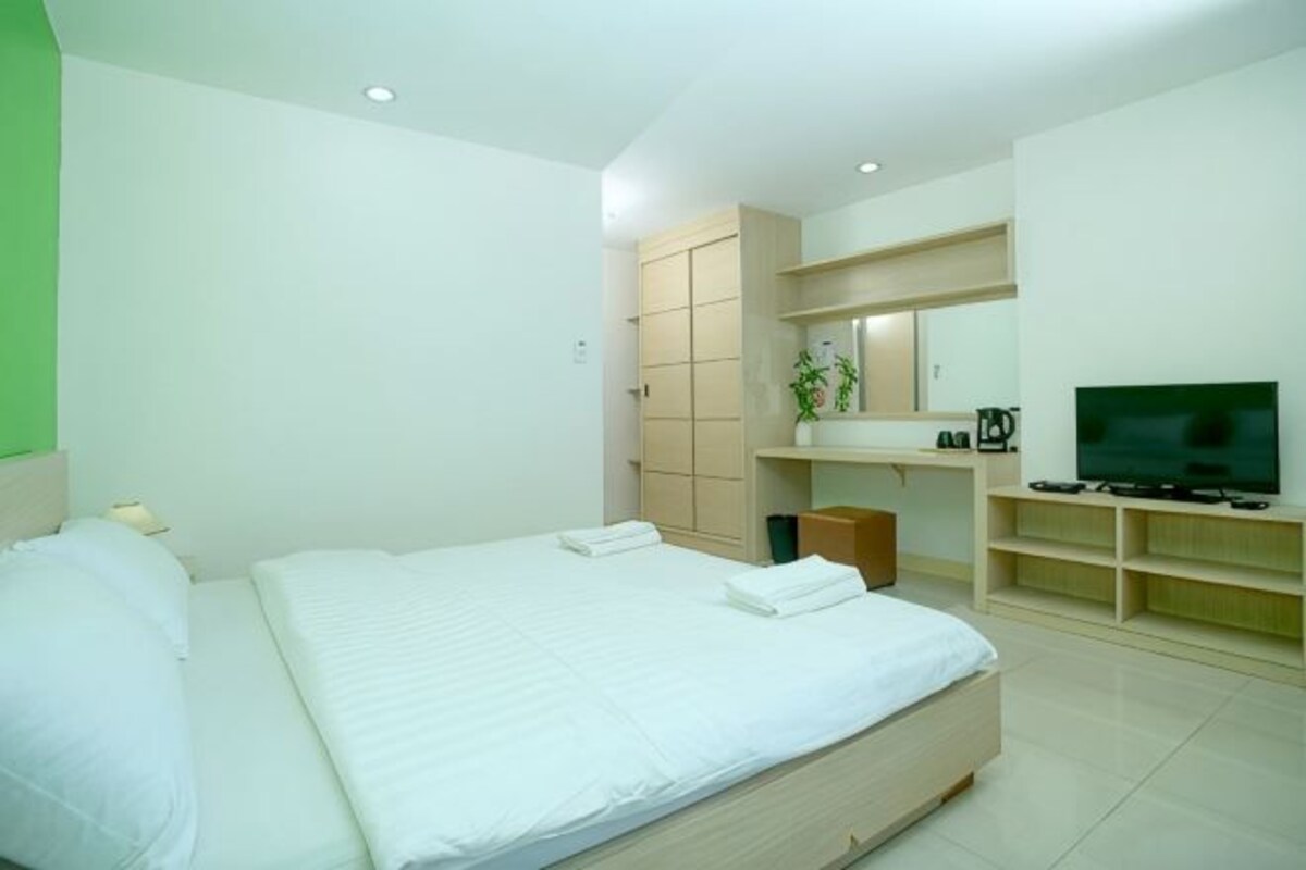 A modern hotel room with a large bed, a TV, a desk, and a bathroom.