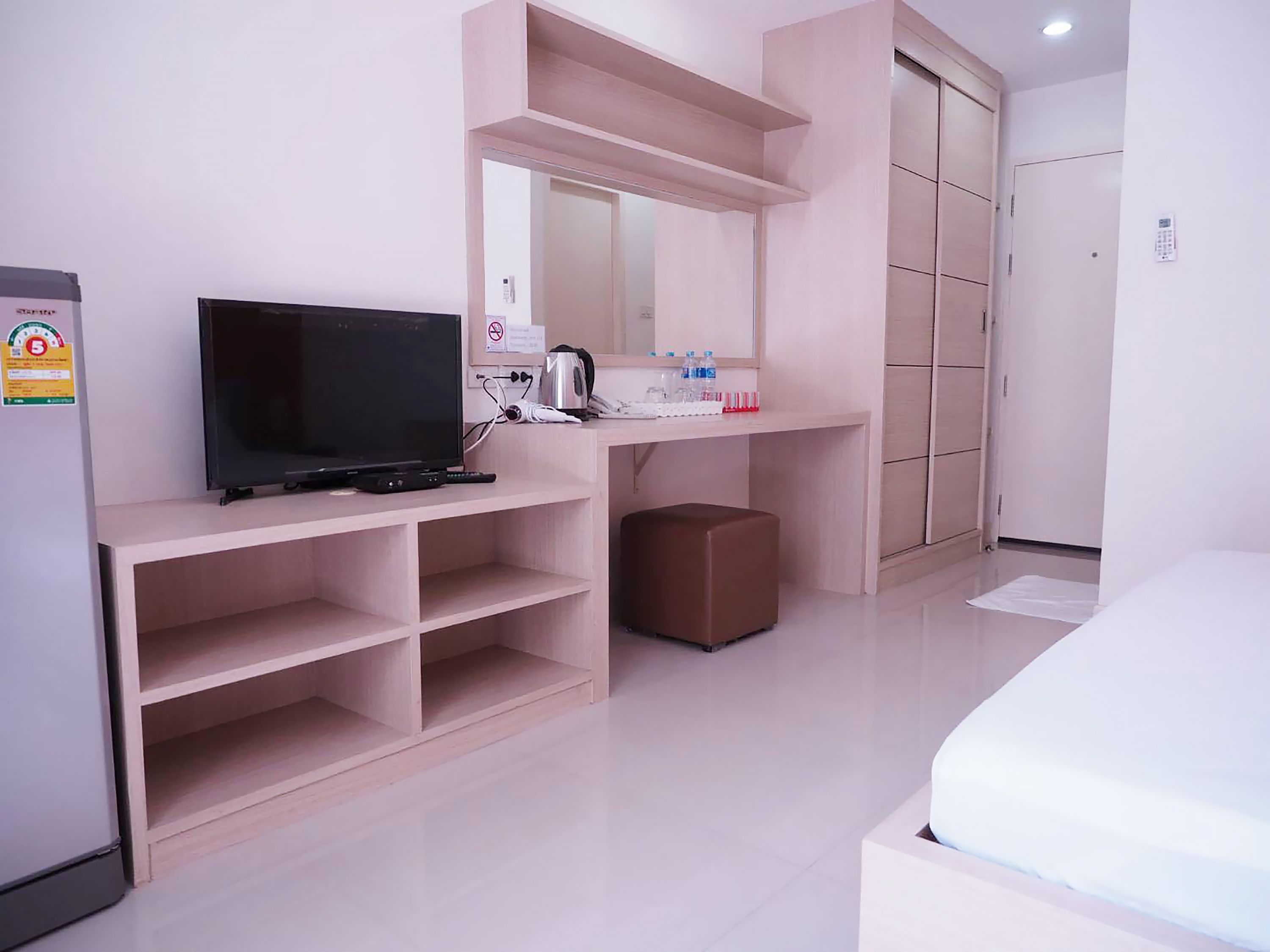 A modern hotel room with a flat-screen TV, a small kitchenette, a wardrobe, and a bed.
