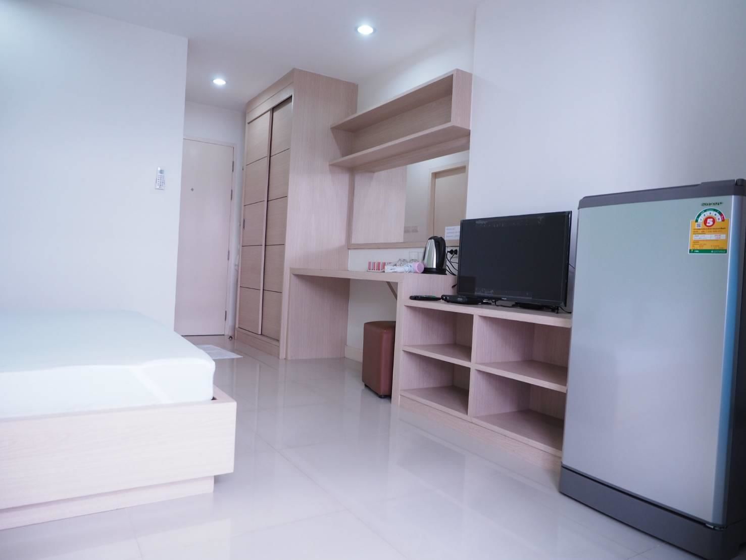 A compact room with a bed, a desk with a computer, a refrigerator, and built-in shelving.