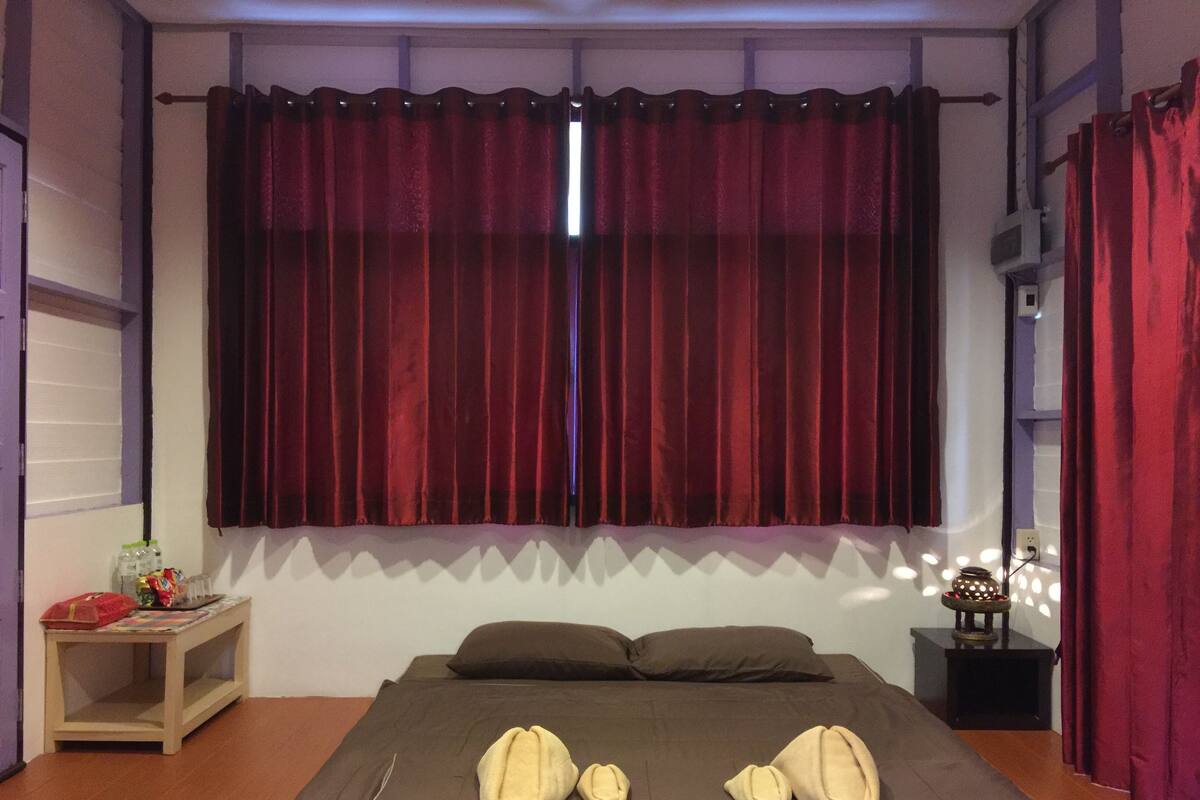 Quarto com cama grande, mesa de cabeceira, abajur e janela com cortinas vermelhas.