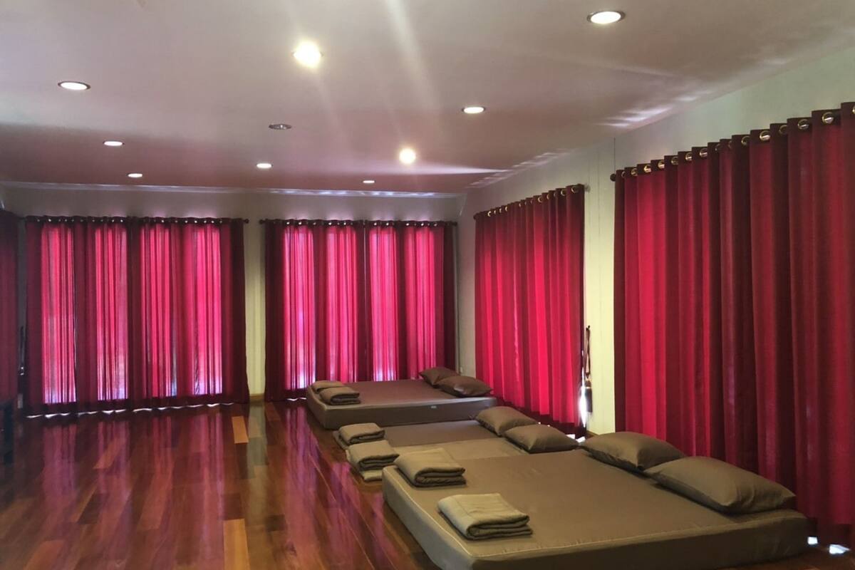 Quarto com piso de madeira, cortinas vermelhas e cama com almofadas e toalhas dobradas.