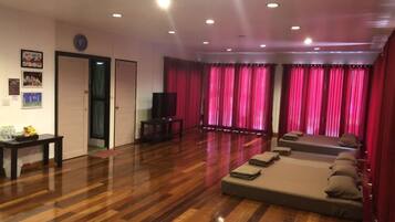 A spacious living room with a wooden floor, a sofa set, a television, and red curtains.