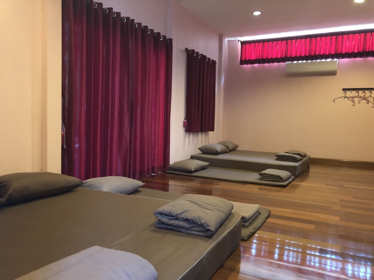 A room with a bed, two small beds, and a window with red curtains.
