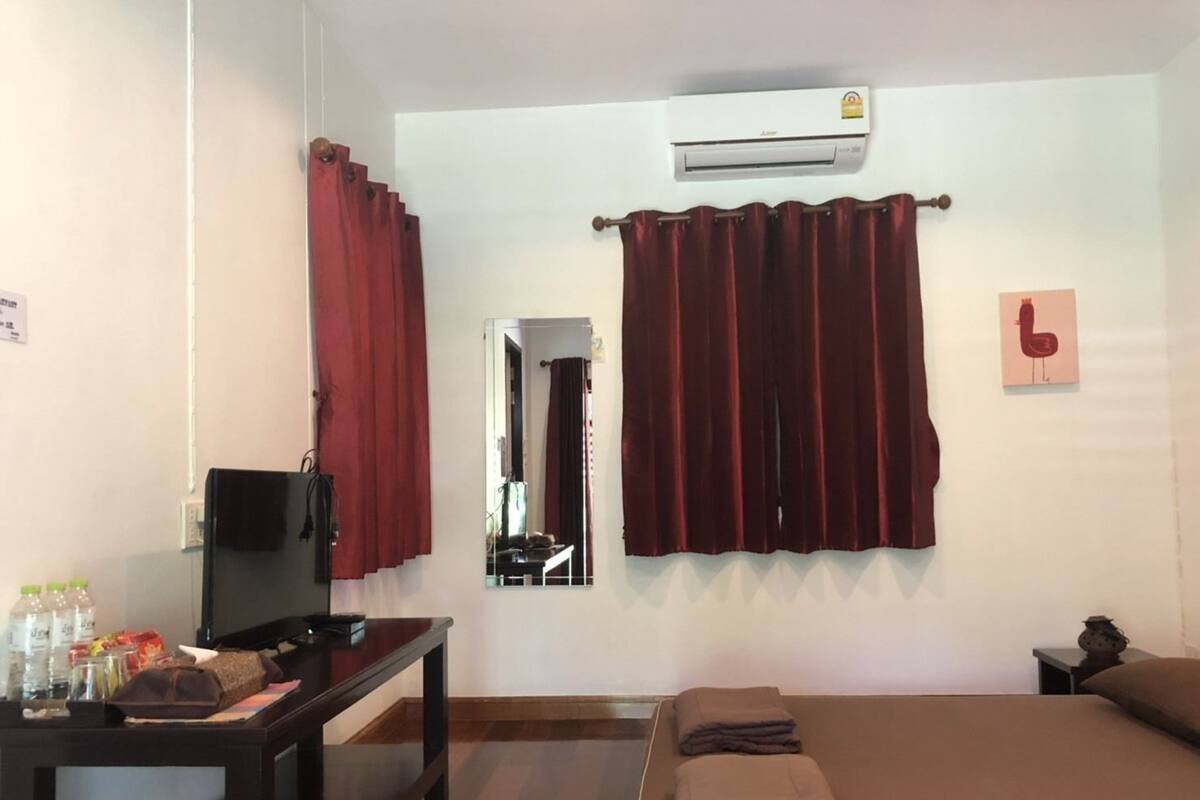 Quarto de hotel com cama, escrivaninha com televisão, espelho e ar condicionado.