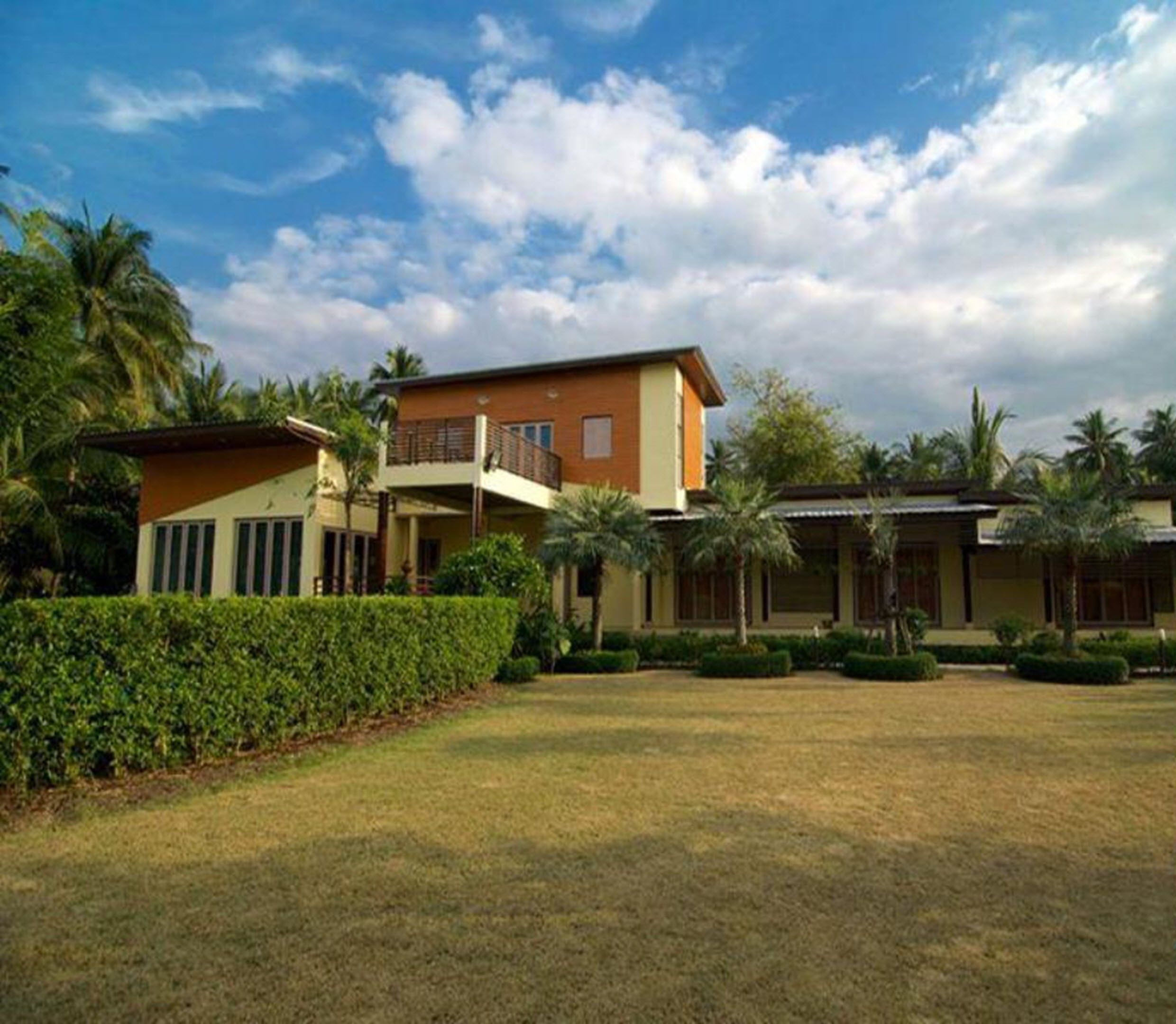 A two-story house with a balcony, surrounded by a well-maintained lawn and palm trees.