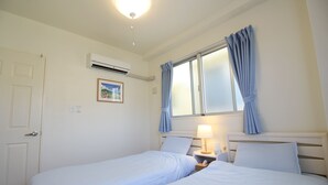A hotel room with two single beds, a window with curtains, an air conditioning unit, and a bedside table with a lamp. - JQ Villa Okinawa Yaka (Kin)