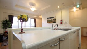 A modern kitchen with a white countertop, stainless steel sink, and a vase with yellow flowers. - JQ Villa Okinawa Yaka (Kin)