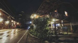 A nighttime street view with a building featuring a thatched roof and illuminated windows. - Maekampong Kidteng (Mae On)