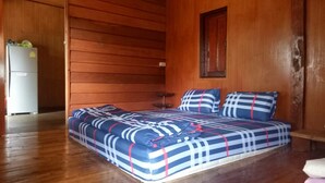 A bedroom with a bed, wooden walls, a small window, and a refrigerator. - Maekampong Kidteng (Mae On)