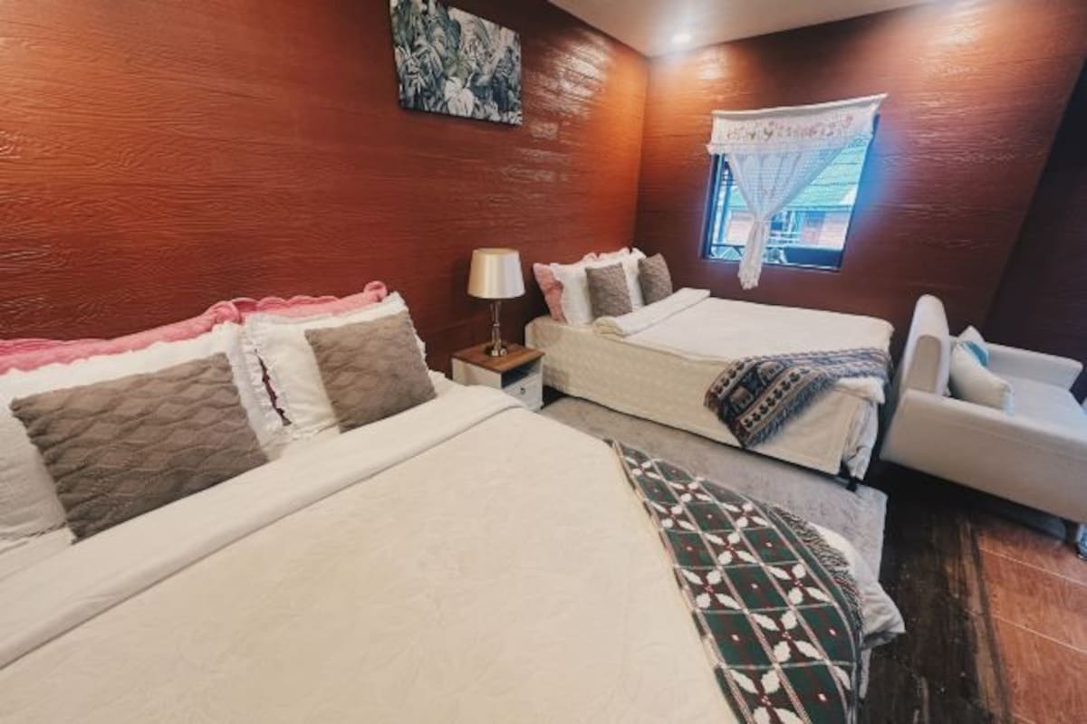 A bedroom with two beds, a nightstand, a window with a curtain, and a wall painting.