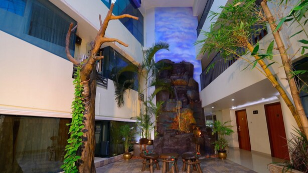 Ein Hotel-Atrium mit einem zentralen Felswasserfall, Zimmerpflanzen und einer Sitzecke mit Stühlen.