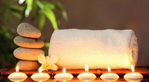 A spa setting with a stack of smooth stones, a rolled towel, and lit candles. - SPS Kings Way (Thiruvananthapuram)