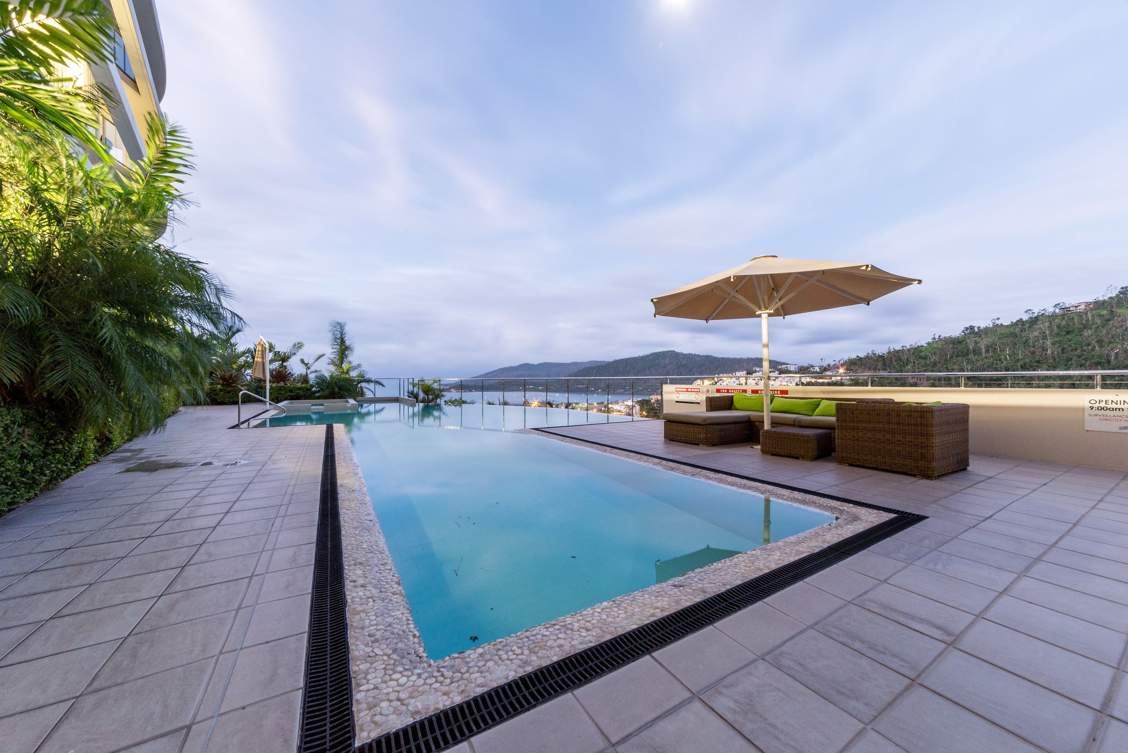 Une piscine avec vue sur la mer, entourée d’une terrasse carrelée et de mobilier d’extérieur.