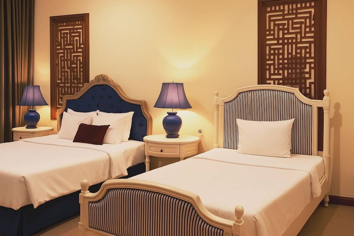A hotel room with two beds, each with a headboard and bedside tables.