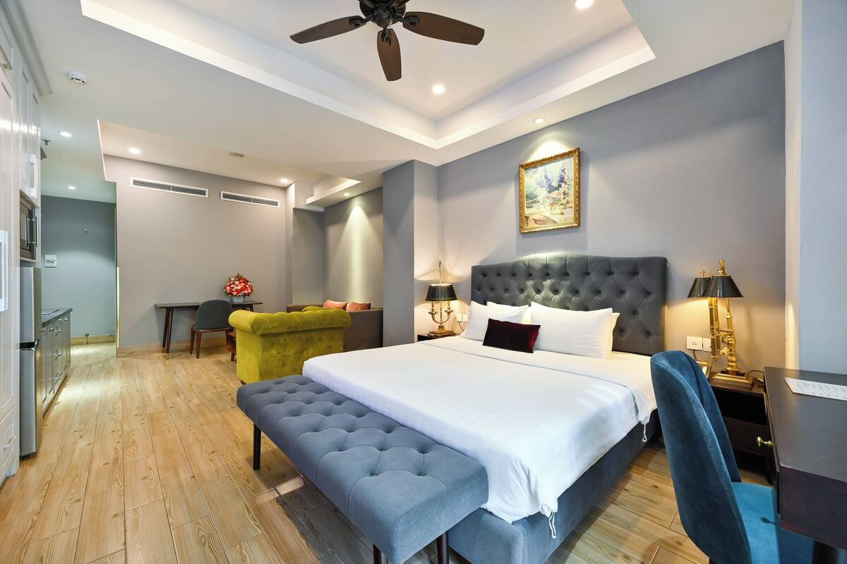 A modern hotel room with a large bed, a desk, a chair, and a bench.