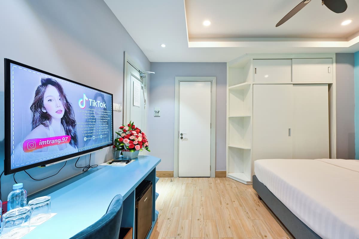 A modern hotel room with a flat-screen TV on a blue console, a bed, a wardrobe, and a door with a white doorbell.