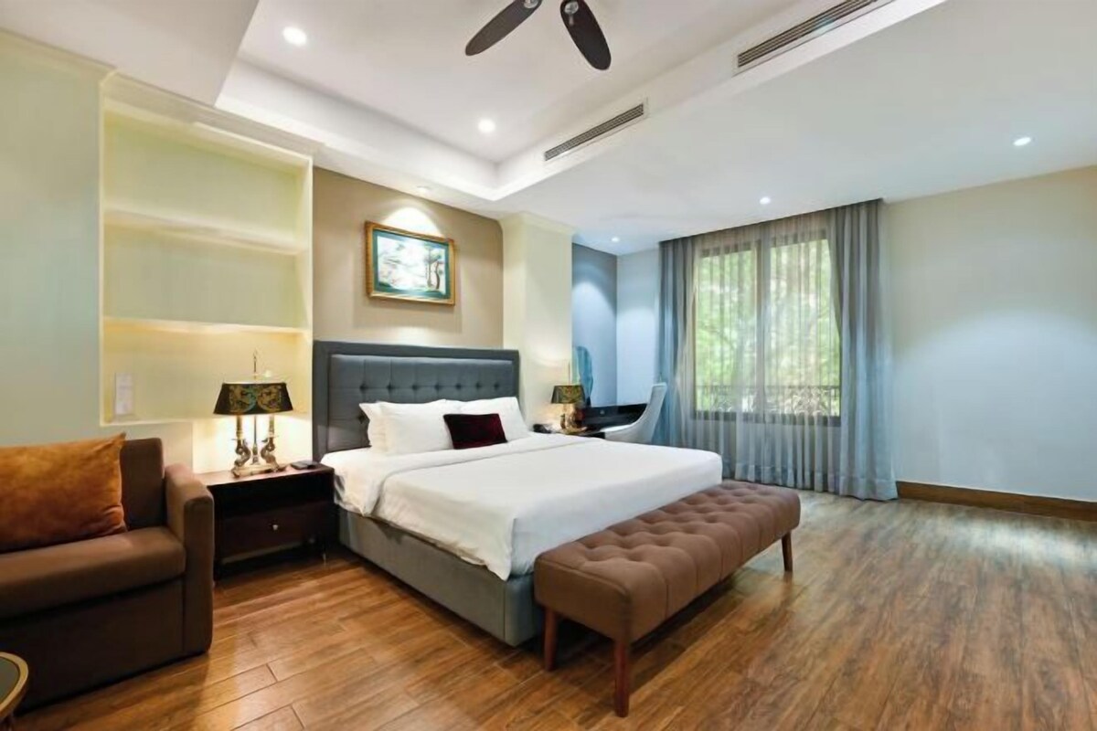 Una habitación de hotel moderna con una cama grande, un sofá, un banco, un escritorio y una ventana con cortinas.