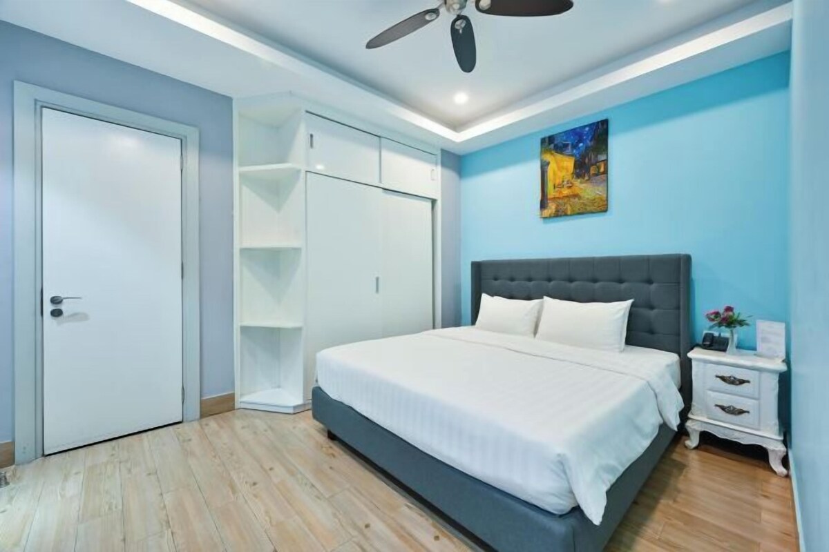 Un dormitorio con cama, ventilador de techo, mesita de noche y un cuadro en la pared.
