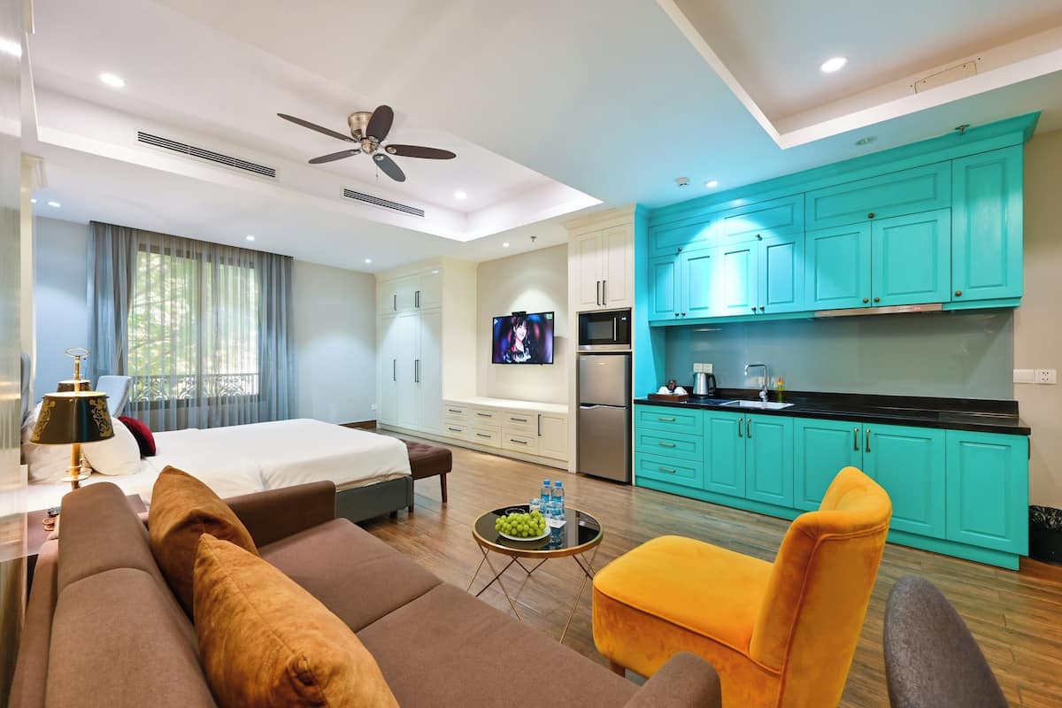 A modern hotel room with a bed, sofa, armchair, and a small table with a fruit bowl.