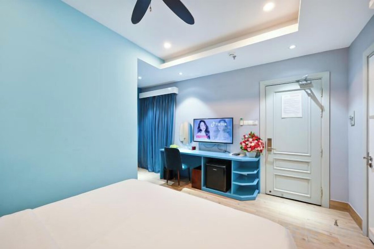 A hotel room with a bed, a desk with a computer, a television, and a door.