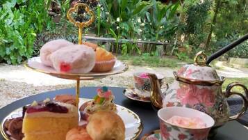 Un présentoir à trois niveaux, garni de pâtisseries et surmonté d’une théière, est posé sur une table à l’extérieur.