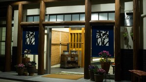 A traditional Japanese building with wooden pillars and sliding doors, featuring a small entrance area with potted plants and a wooden bench. - Gensen no Yado Maruishi Ryokan (Hakuba)