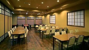 A conference room with multiple tables and chairs, large windows, and a wooden floor. - Gensen no Yado Maruishi Ryokan (Hakuba)