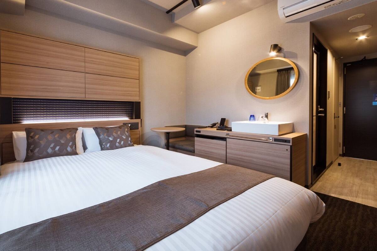 Une chambre d’hôtel moderne avec un lit, une table de chevet et un miroir rond.