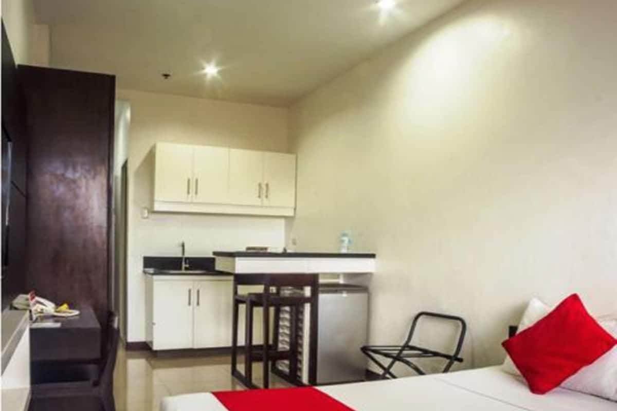 Ein kleines Hotelzimmer mit Bett, Schreibtisch und einer Küchenzeile.