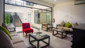Una hall moderna con una scala, un'area salotto e porte in vetro che conducono a un corridoio.