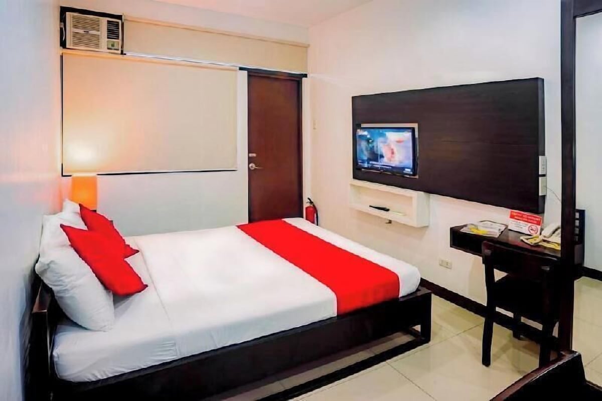 A hotel room with a bed, a TV, a desk, and a chair.