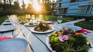 Una mesa de picnic al aire libre con platos de comida, vasos y cubiertos.