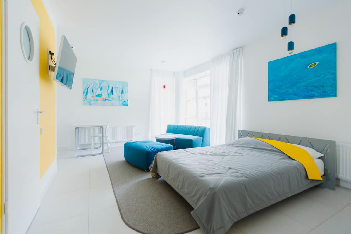 A modern bedroom with a bed, a blue chair, a round table, and artwork on the walls.